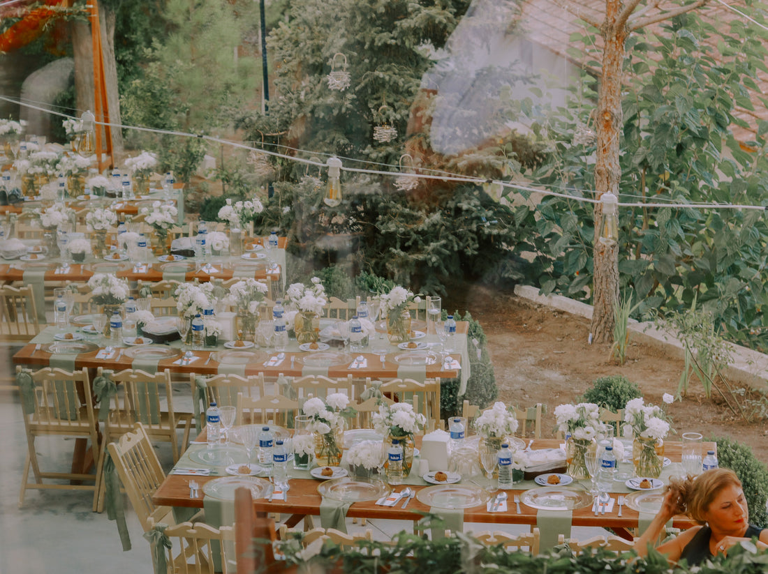Long outdoor reception tables dressed with sage green fabric table runners and place settings