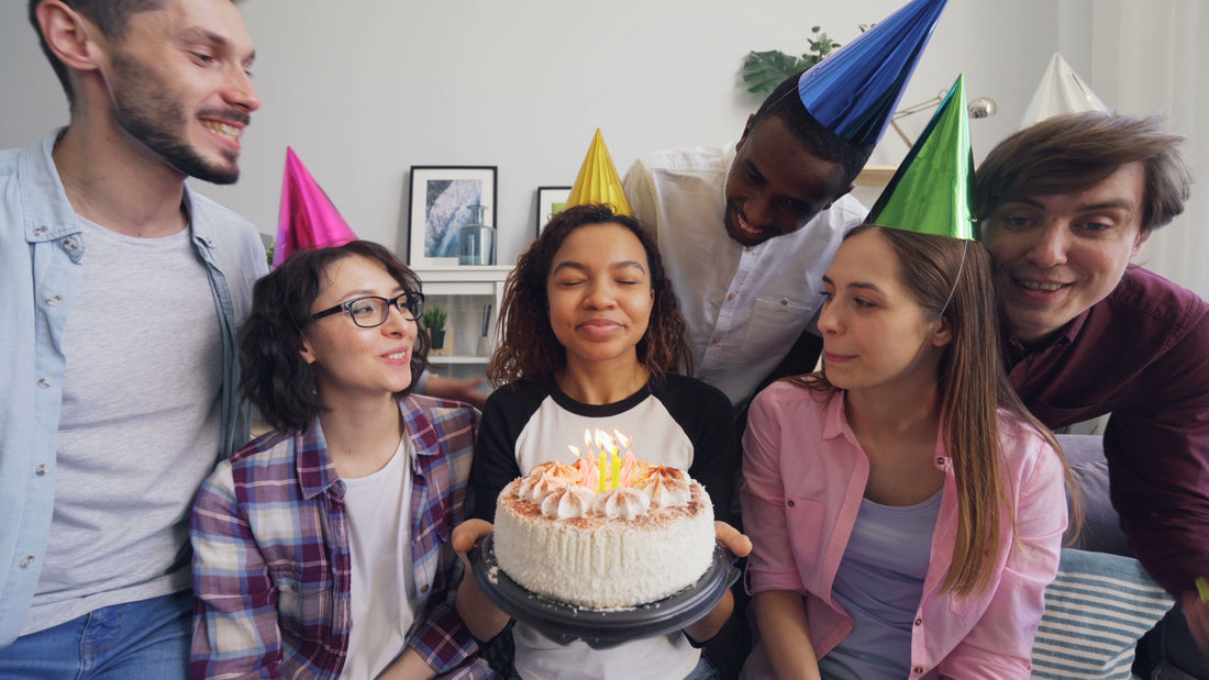 Group of adult friends celebrating a birthday together at home with a cake