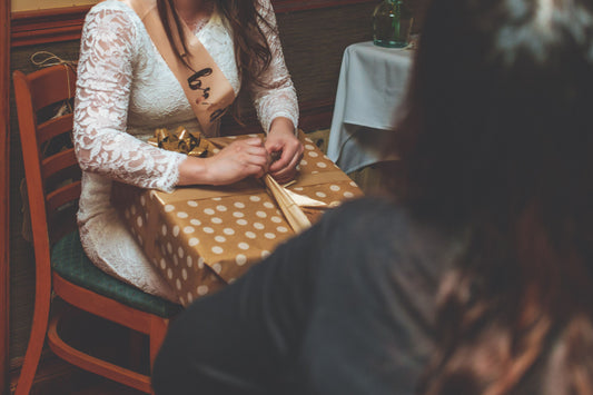 Bridal shower guest of honor in a lace dress and sash unwrapping a wrapped gift