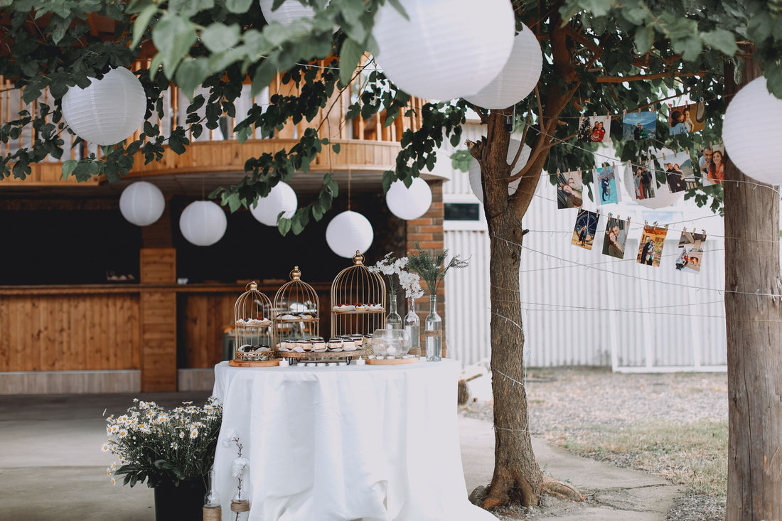 White paper lanterns hanging at varied heights over an outdoor party dessert table