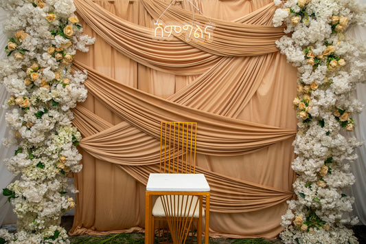 Elegant draped fabric backdrop with floral arch, styled for an indoor party celebration
