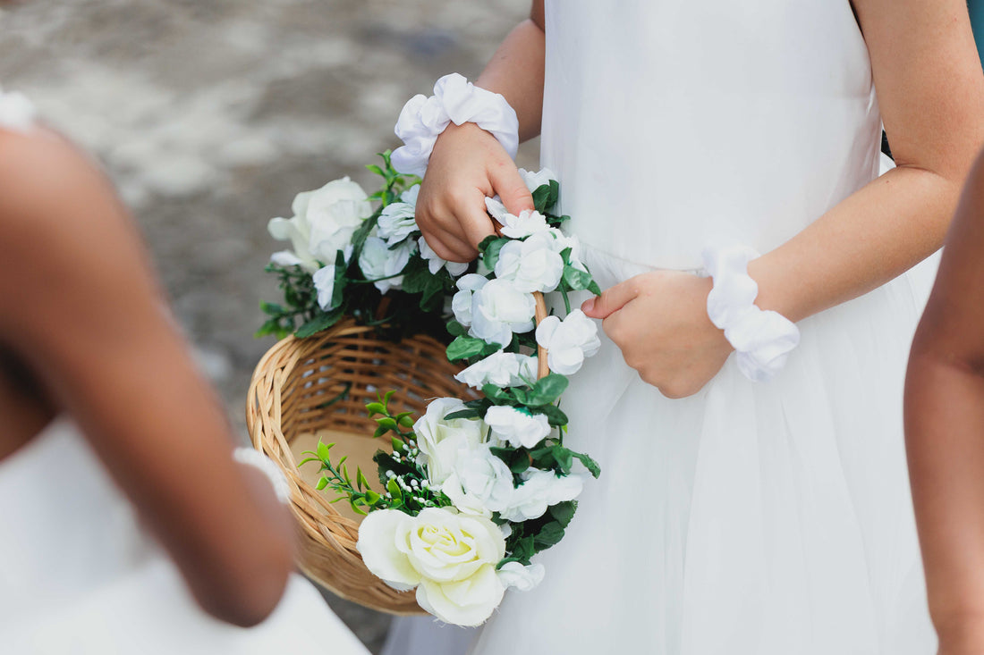 Child carrying a wicker flower girl basket with white roses at an outdoor wedding ceremony