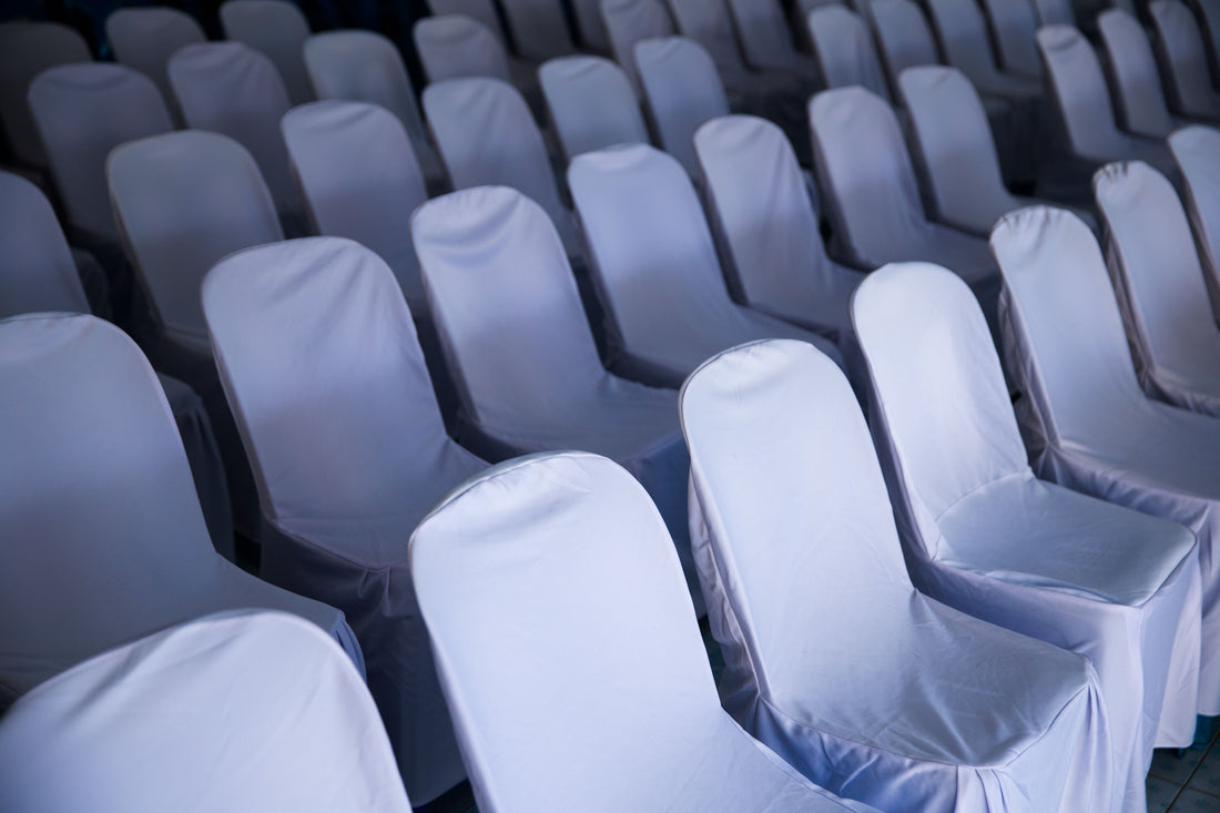 Rows of fitted white chair covers set up for an indoor celebration