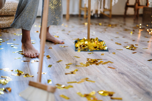 Woman sweeping up confetti after a party at home, tidying a wood floor with a broom and dustpan