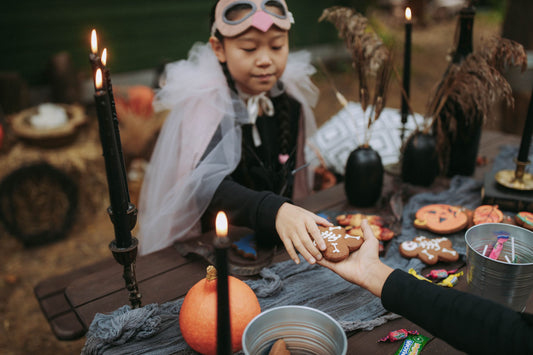 Costumed child receiving a Halloween treat from an adult at a decorated outdoor table