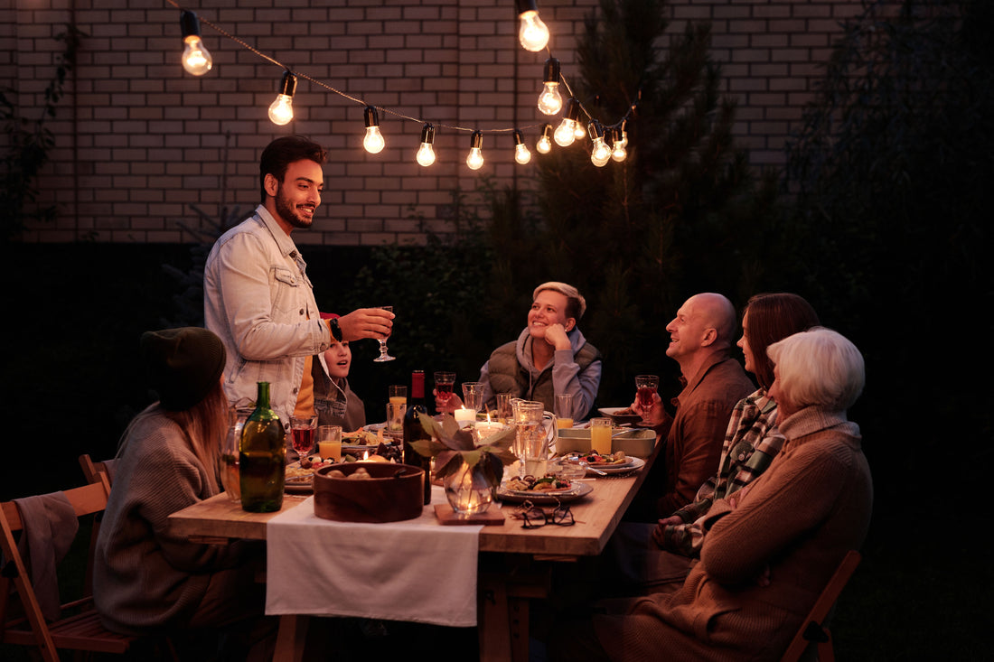 Family and friends enjoying an evening backyard dinner under warm overhead string lights