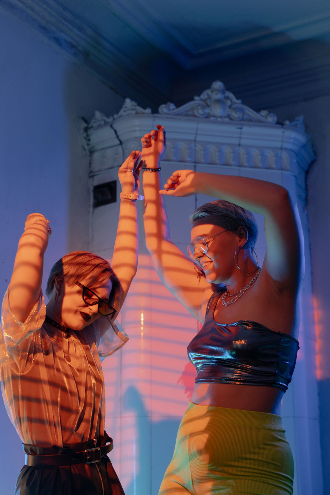 Two friends dancing in a lived-in apartment room with colorful reflected light