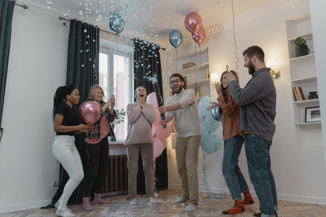 Friends laughing and reacting candidly to a balloon color-pop reveal in a home living room