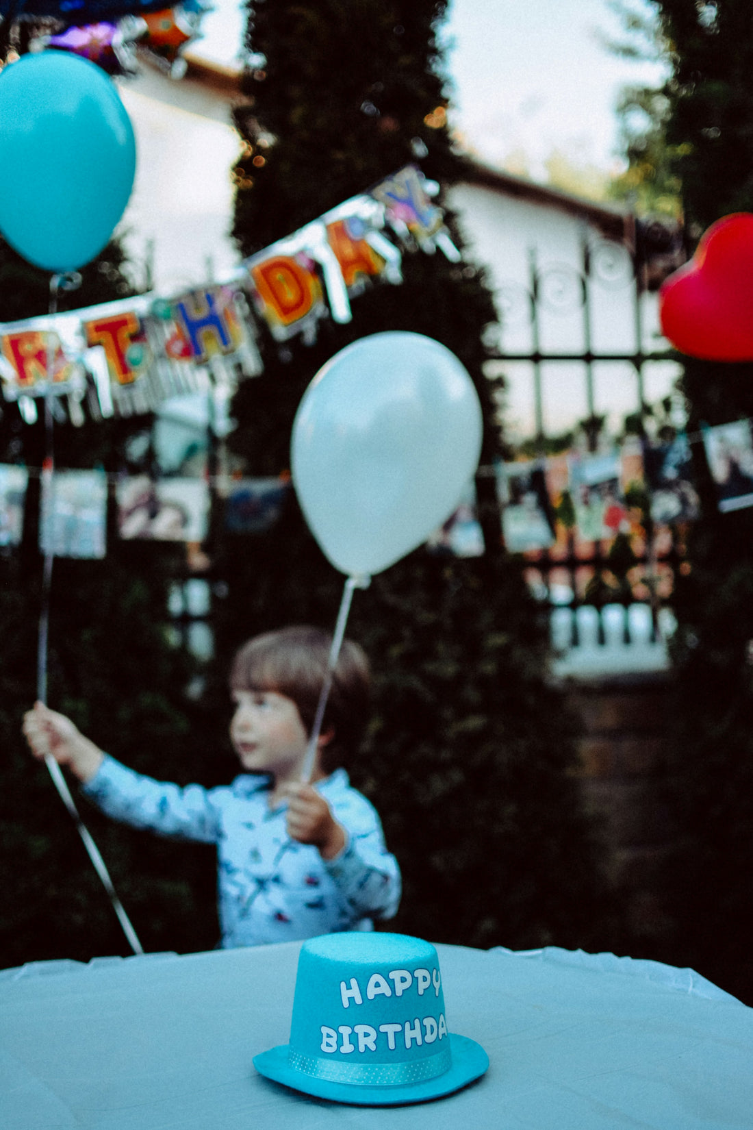 Young boy holding balloons at an outdoor birthday party with a happy birthday banner