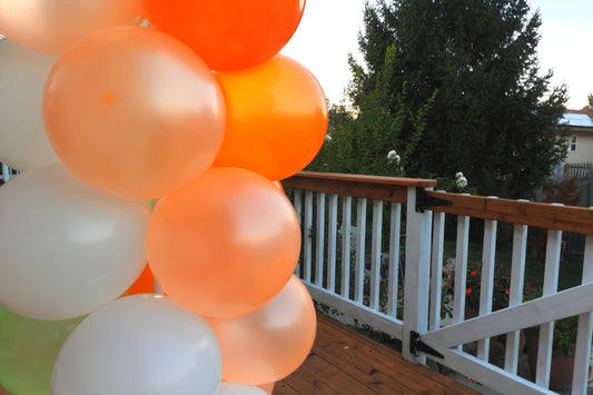 Compact cluster of orange and white balloons decorating a home deck corner at dusk for a Halloween gathering