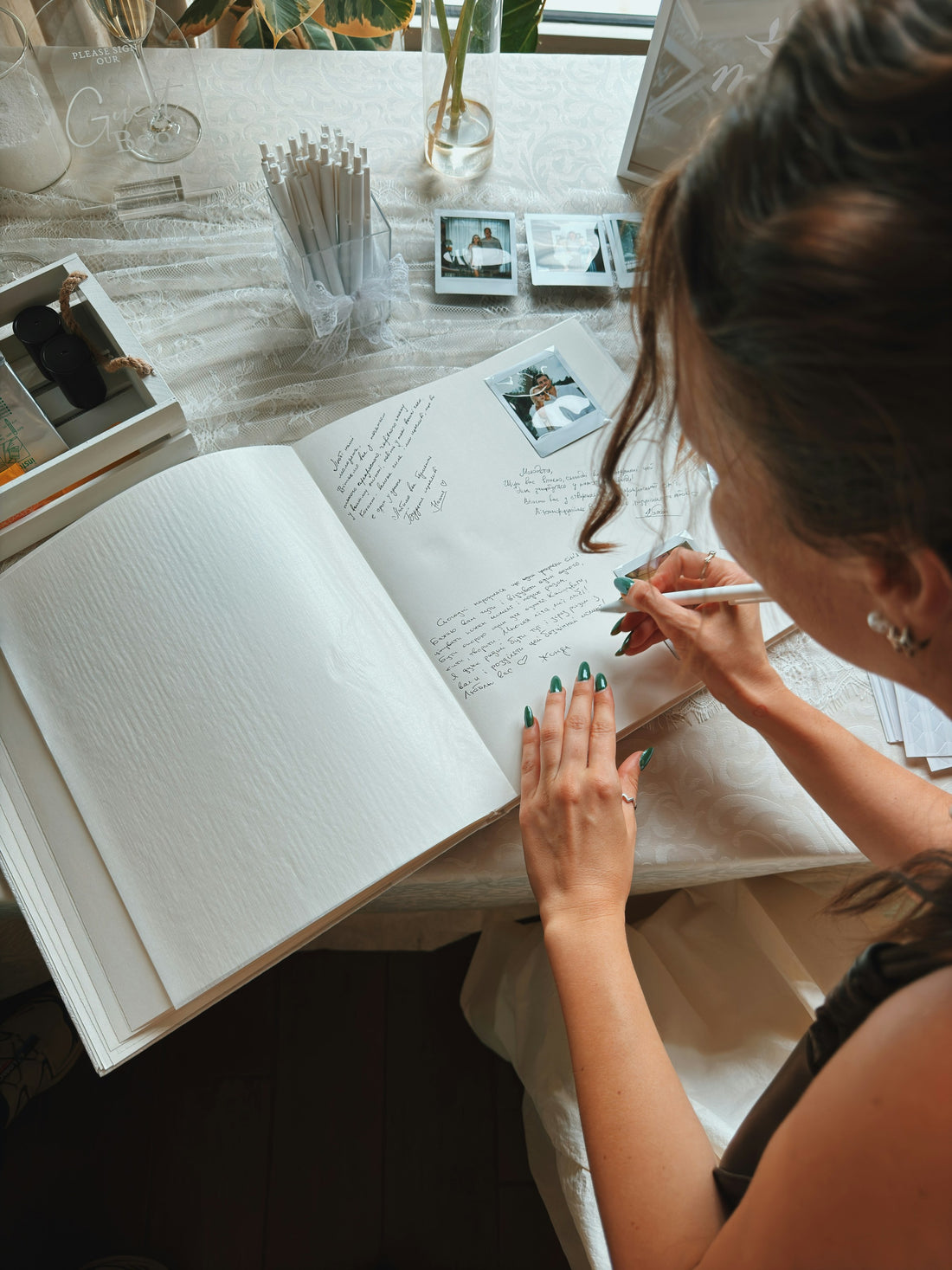 Wedding guest writing a message in a guestbook surrounded by photo keepsakes